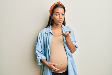 Sticker - Beautiful hispanic woman expecting a baby, touching pregnant belly looking at the camera blowing a kiss with hand on air being lovely and sexy. love expression.