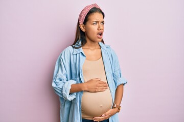 Sticker - Beautiful hispanic woman expecting a baby, touching pregnant belly angry and mad screaming frustrated and furious, shouting with anger. rage and aggressive concept.