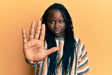 Poster - Young black woman with braids wearing casual winter sweater doing stop sing with palm of the hand. warning expression with negative and serious gesture on the face.