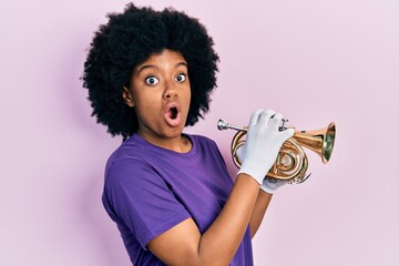 Canvas Print - Young african american woman playing trumpet afraid and shocked with surprise and amazed expression, fear and excited face.