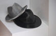 Conjunto de dois chapéus pousados em cubos de acrílico brancos, um chapéu cinzento e outro preto, acessórios de moda