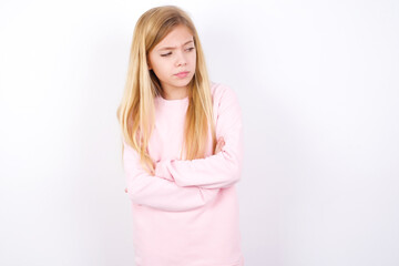 Displeased beautiful caucasian little girl wearing pink hoodie over white background with bad attitude, arms crossed looking sideways. Negative human emotion facial expression feelings.