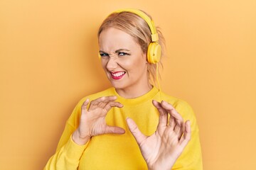 Canvas Print - Young blonde woman listening to music using headphones disgusted expression, displeased and fearful doing disgust face because aversion reaction. with hands raised