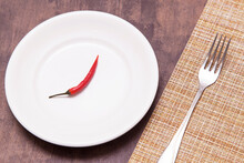 Single One Red Chili Pepper On Empty White Plate And Fork On Table. Spicy Asian Food Concept