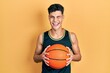 © Krakenimages.com - Young hispanic man holding basketball ball winking looking at the camera with sexy expression, cheerful and happy face.