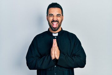 Sticker - Handsome hispanic priest man with beard standing over isolated background sticking tongue out happy with funny expression.