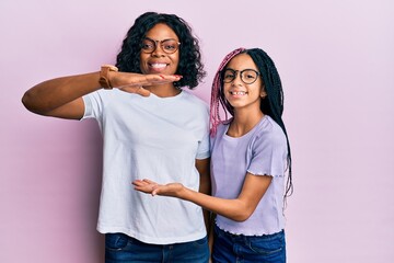 Canvas Print - Beautiful african american mother and daughter wearing casual clothes and glasses gesturing with hands showing big and large size sign, measure symbol. smiling looking at the camera. measuring