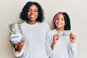 Poster - Beautiful african american mother and daughter holding jar with savings and 1 dollar banknote smiling with a happy and cool smile on face. showing teeth.