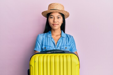 Sticker - Young chinese woman wearing summer hat and holding cabin bag with a happy and cool smile on face. lucky person.