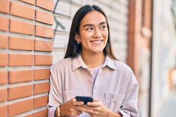 Poster - Young latin girl smiling happy using smartphone at the city.