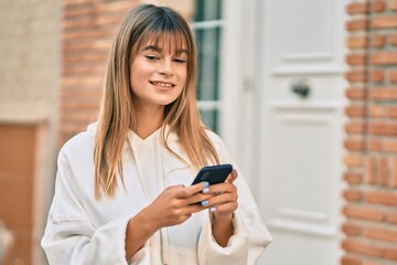 Caucasian sporty teenager girl smiling happy using smartphone at the city.