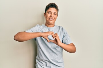 Wall Mural - Teenager hispanic boy wearing casual grey t shirt smiling in love doing heart symbol shape with hands. romantic concept.