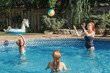 Mother playing ball with daughters children in swimming pool on home backyard. Mom and sisters siblings having fun in swimming pool together. Summer outdoor water activity for family and kids.