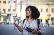 © liderina - Woman with camera standing on street and drinking coffee.