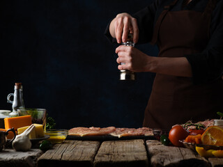 Wall Mural - Cooking chicken fillet for grilling or BBQ. Chef peppers, freezing chicken in motion on a background of vegetables