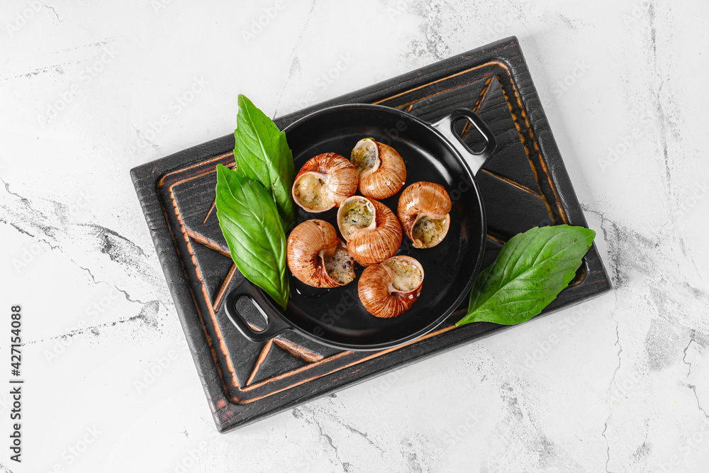 Frying pan with tasty snails on light background
