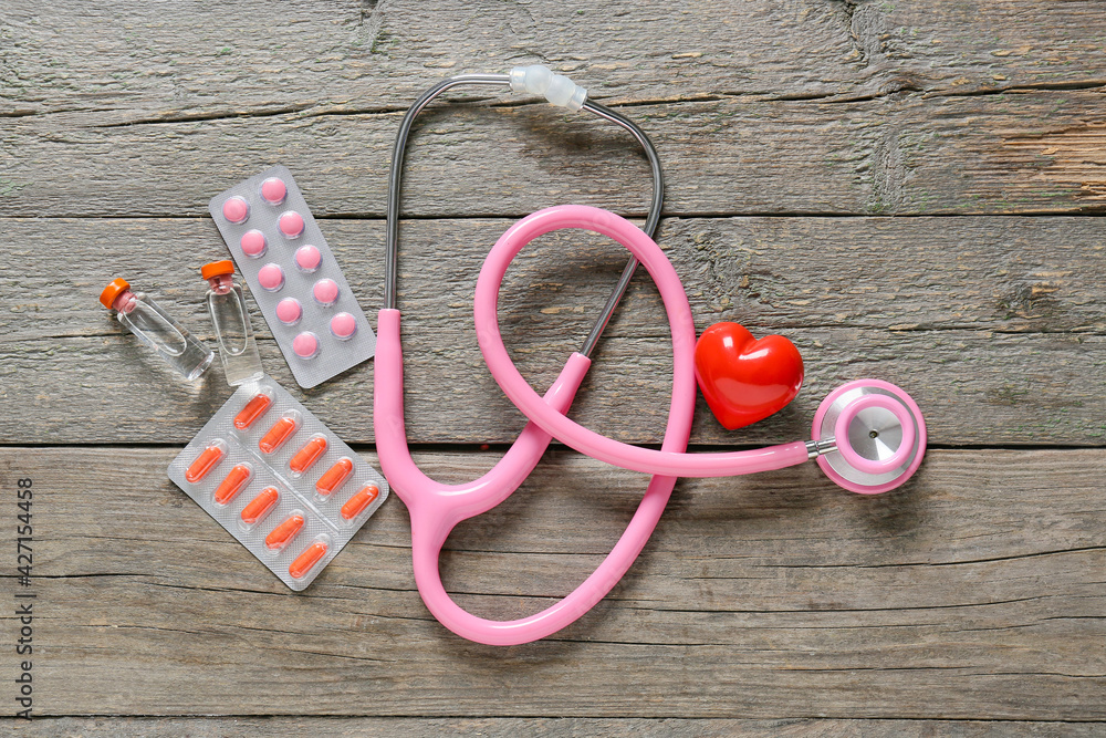 Modern stethoscope, medicines and heart on wooden background