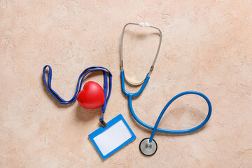 Modern stethoscope, blank badge and heart on color background