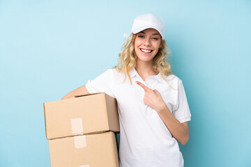 Canvas Print - Young delivery woman isolated on blue background pointing finger to the side