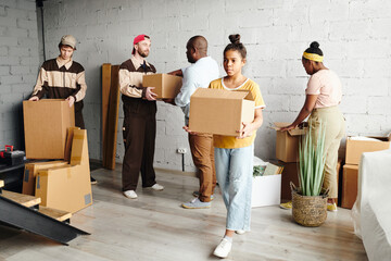 Wall Mural - Pretty teenage girl of African ethnicity carrying packed cardboard box while helping her father and mother with removing to new flat or house