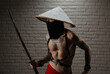 samurai man in a red cape and an Asian triangular hat with tattoos and a katana sword in his hands against the background of a brick wall
