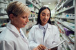 © StratfordProductions - Two female pharmacists discussing in chemist using digital table while standing between aisle