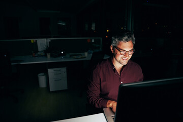 Portrait of a smiling businessman working on a computer at his office desk late into the night