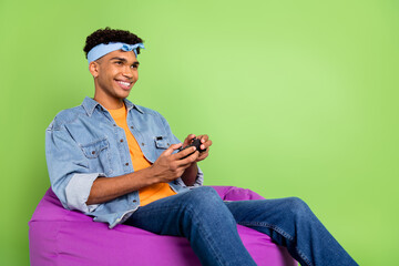 Poster - Photo of guy sit beanbag hold controller look empty space wear headband denim shirt isolated green color background