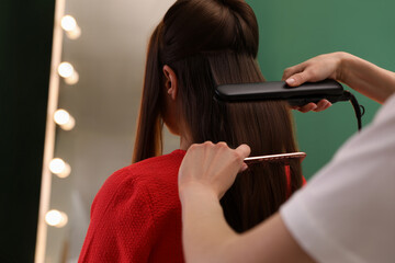 Stylist straightening woman's hair with flat iron in salon