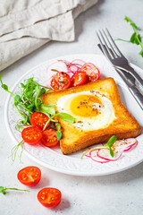 Canvas Print - Fried egg in bread toast with tomatoes, radishes and sprouts on white plate, gray background. Healthy breakfast concept.