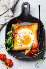 Canvas Print - Fried egg in toast bread with tomatoes and sprouts in black frying pan, top view.