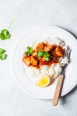 Canvas Print - Fried chicken in tomato sauce with rice on white plate, gray background, top view.