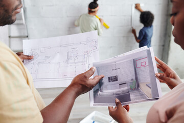 Canvas Print - Hands of young African couple looking through and discussing papers with draft and interior of living-room against their children standing by wall