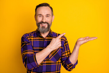 Sticker - Photo portrait of smiling aged man wearing plaid pointing finger holding hand copyspace isolated on vibrant yellow color background