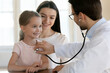© fizkes - Young male pediatrician hold stethoscope listen to happy small kid girl heart at checkup visit at hospital with mom. Caring man doctor use phonendoscope check lungs breath of little kid in clinic.