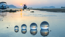 The Sun Rises Within The Glass Beads Arranged In A Shallow Canal, .the Water Gently Flows Through The Orb Into The Sea. .A Crystal Sphere Revealing The Upside-down Sunrise Sea View.
