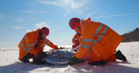 Paramedics in orange workwear examining unconscious woman before getting her to hovercraft