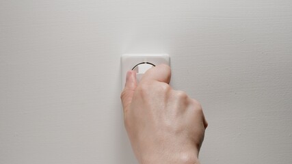 Human hand inserts a plug into an electrical outlet on a white wall