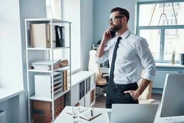 Sticker - Handsome young man in formalwear talking on the phone and smiling while working in the office