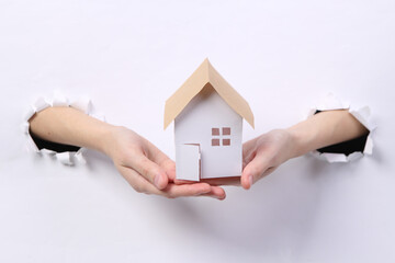 Wall Mural - Female hands holding house figure through torn hole white paper.