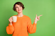 © deagreez - Photo of happy trendy young woman look point index finger empty space hold mug coffee isolated on green color background