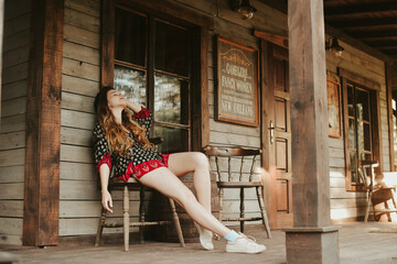 Wall Mural - A woman is resting on a terrace near a western house, a weekend in an interesting hotel. Travel alone. Long-legged woman resting after work on the farm.