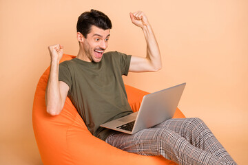 Poster - Photo of hooray brunet guy sit look laptop wear t-shirt trousers isolated on beige color background