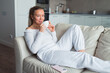 © shapovalphoto - Woman drink coffee lay on sofa at home, white suit, relax, well being , me time concept