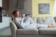 © shapovalphoto - Woman drink coffee lay on sofa at home, white suit, relax, well being , me time concept