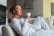 © shapovalphoto - Woman drink coffee lay on sofa at home, white suit, relax, well being , me time concept