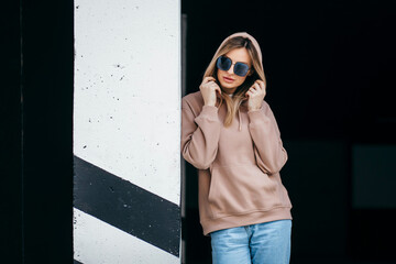 Wall Mural - Fasion blonde woman in brown oversize hoodie, glasses and blue jeans, mockup for logo or branding design