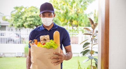 Wall Mural - Delivery African man employee wearing face mask blue cap uniform mask hold paper bag packet organic food at home front door. Service quarantine pandemic. Express grocery delivery service courier.