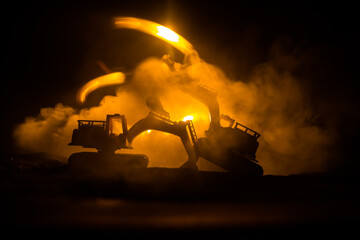 Construction site on a city street. A yellow digger excavator parked during the night on a construction site. Industrial concept table decoration on dark foggy toned background.