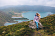 © Ivan - A woman sits on a stone against the backdrop of the beautiful crater of Lake Lagoa do Fogo in the Agua de Pau Massiva stratovolcano in the center of São Miguel Island. Travel to the Azores.